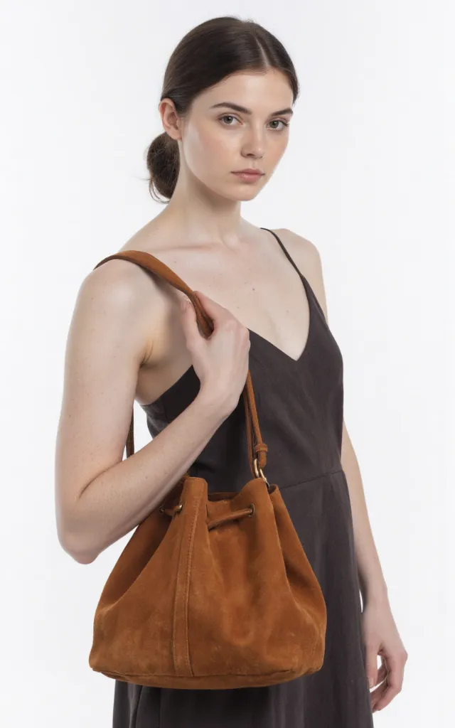 A French female model with a Suede bag, wearing a dress, against a white background, in a front   facing close   up